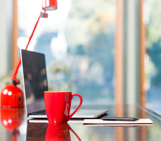 A modern loft space with a desk, laptop, table lamp and red coffee cup.