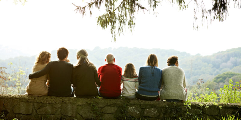 Rear view of multi-generation family relaxing in row on retaining wall against clear sky