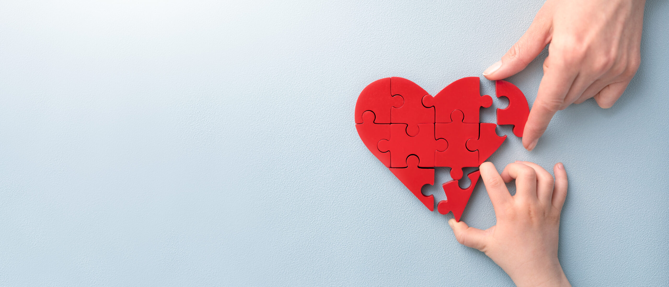 The concept of charity, love, donate and helping hand. International cardiology day. A woman and child arranges red heart shape puzzles. Symbol of helping others.