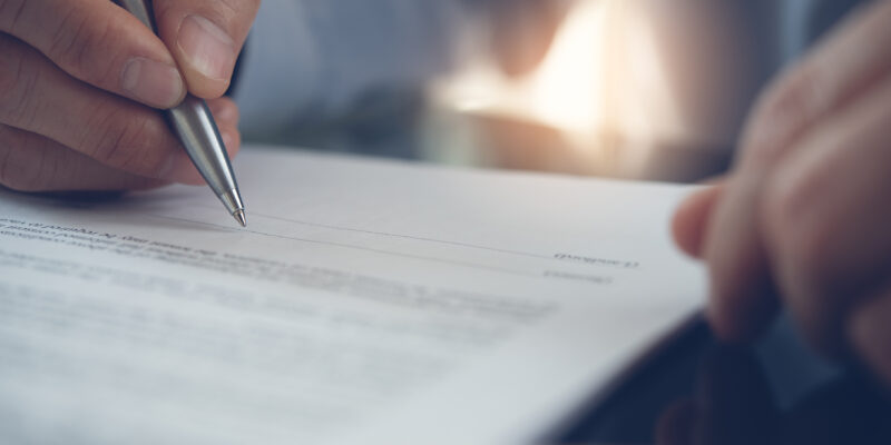 Businessman with pen in hand reading official business contract, rental agreement before making a deal. Man project manager signing document in office, close up.