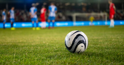 Football kept on grassy football pitch.